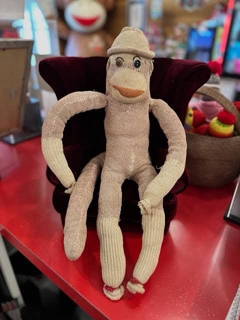 The real Luno, a worn handmade sock monkey in a small knit hat, sitting in a tiny velvet armchair
